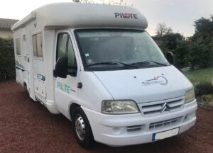 Camping-car Pilote blanc garé sur allée gravillonnée.