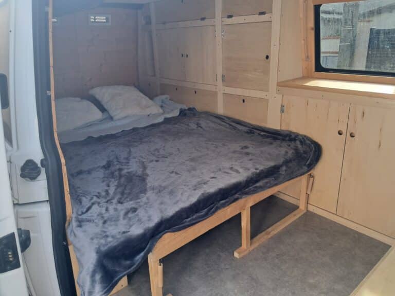 Intérieur aménagé d'un van avec lit et rangement.
