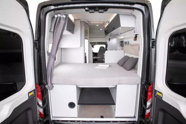 Intérieur d'un fourgon aménagé avec lit et rideau.