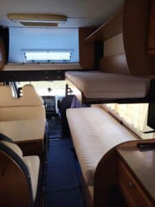 Interno di camper con letto e sedili.