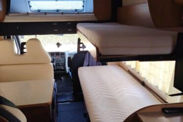 Interno di camper con letto e sedili.