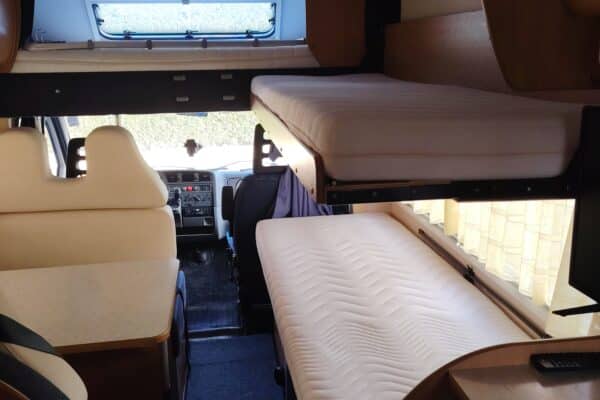 Interno di camper con letto e sedili.