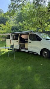 Van aménagé avec auvent dans un parc verdoyant.