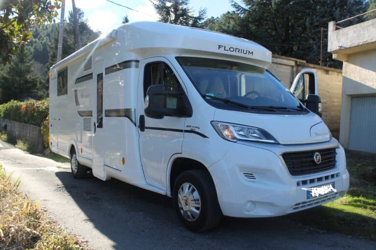Camping-car blanc stationné sur route ensoleillée.