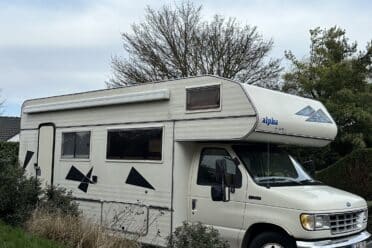 Camping-car blanc stationné sur allée pavée.