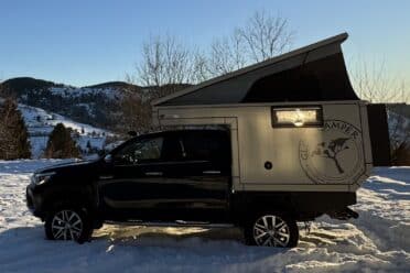 Camionnette avec cellule camper, neige et montagnes en arrière-plan.