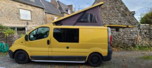 Van jaune avec toit relevable devant maison en pierre.