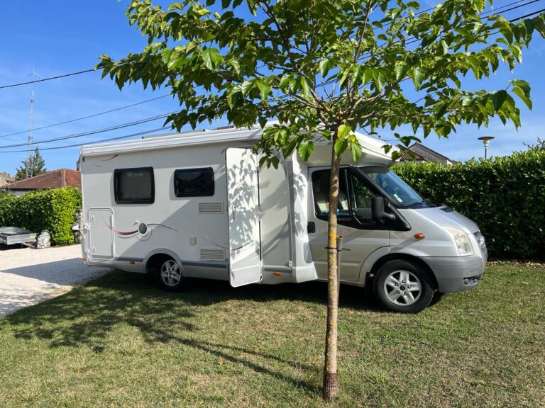Camping-car blanc garé sous un arbre