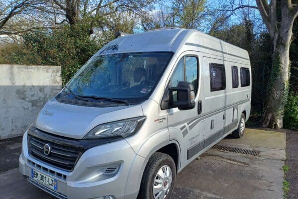 Camping-car gris stationné dans une cour arborée