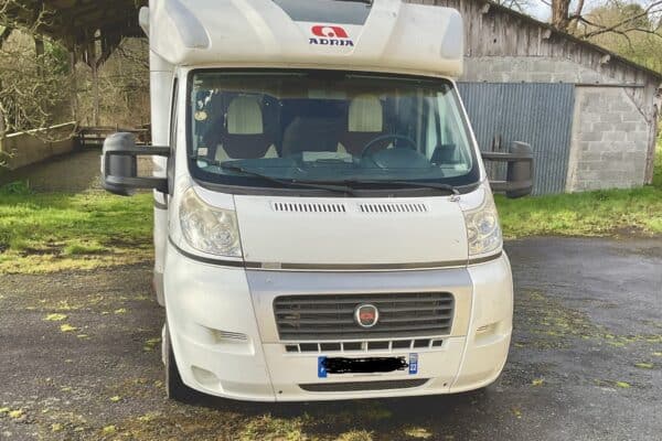 Camping-car Adria blanc stationné devant grange