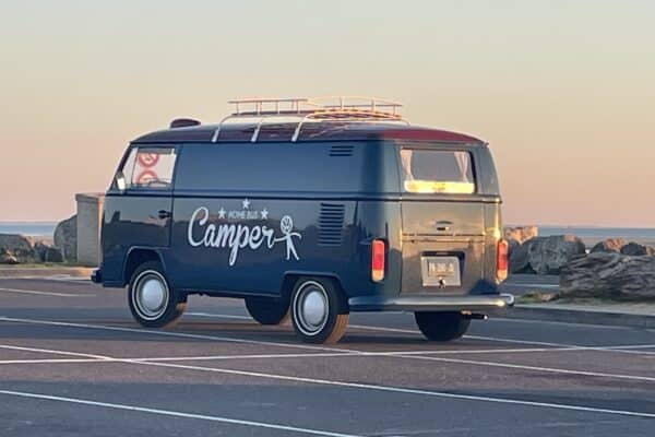 Van aménagé vintage longeant la mer au coucher du soleil