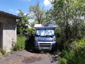 Camping-car stationné entre mur et végétation dense