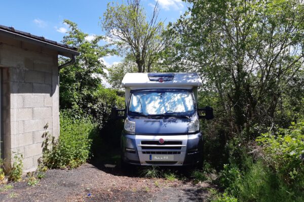 Camping-car stationné entre mur et végétation dense
