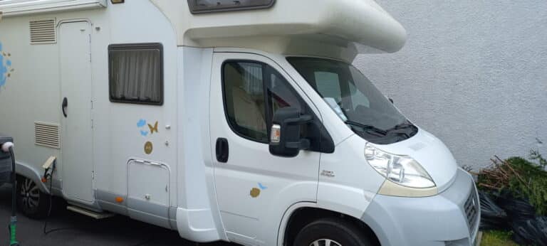 Camping-car blanc branché à une prise électrique