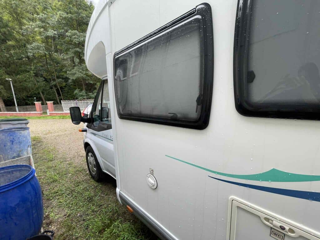 Camping-car blanc garé sous la pluie près d'arbres