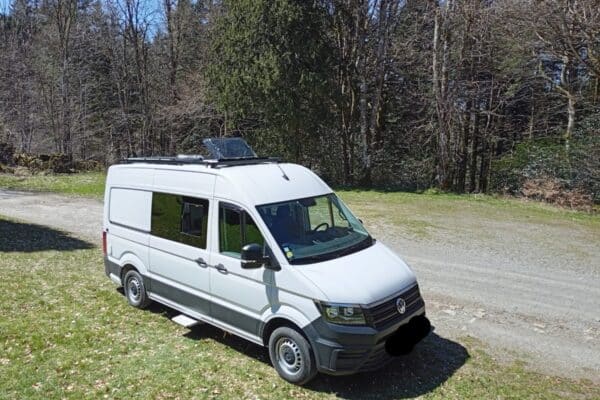Fourgon aménagé blanc garé en lisière de forêt