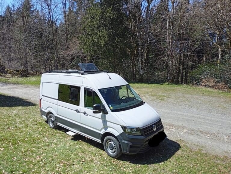 Fourgon aménagé blanc garé en lisière de forêt