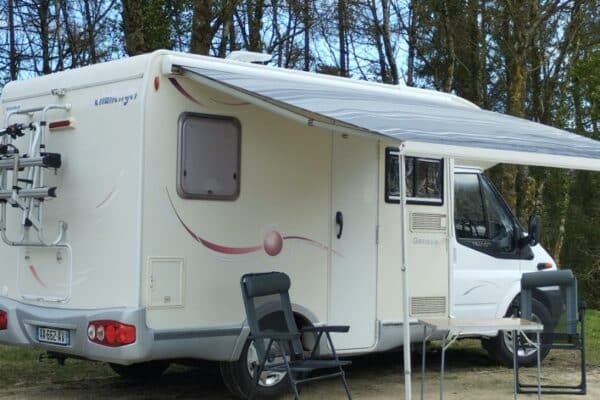 Camping-car mit Vorzelt und Stühlen im Wald