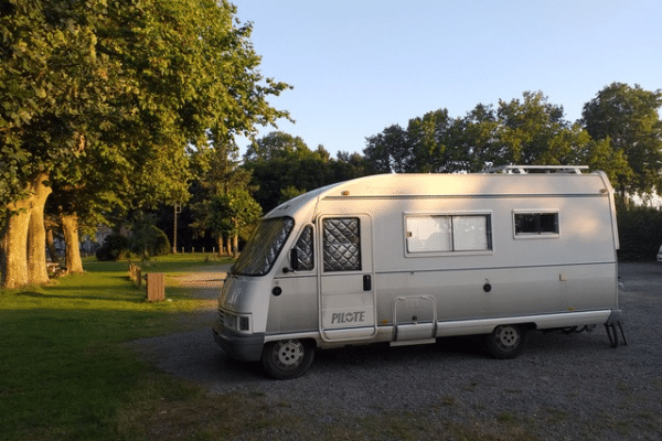 Camping-car blanc stationné près d’arbres au coucher du soleil