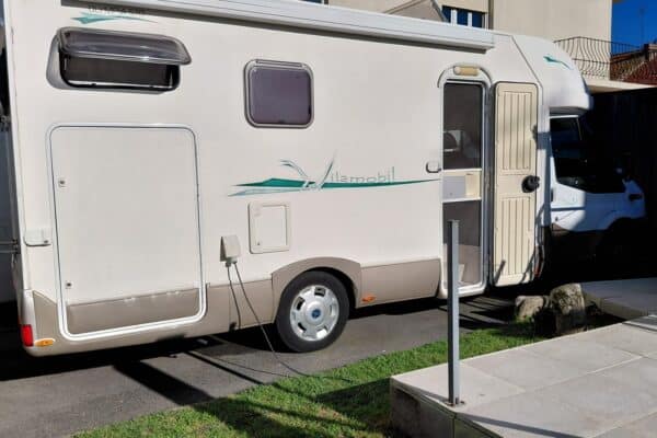 Camping-car stationné devant une maison, branché à l'électricité
