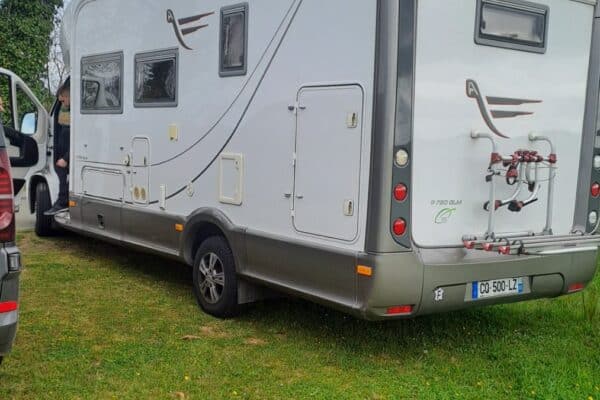 Camping-car blanc garé sur pelouse avec porte-vélos arrière