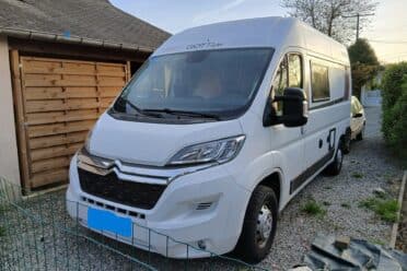 Camping-car blanc stationné devant garage en bois