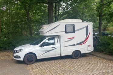 Weißes Wohnmobil auf Parkplatz im Grünen