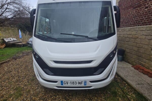 Camping-car blanc stationné dans une cour gravillonnée