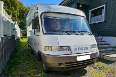Camper bianco parcheggiato vicino a una casa verde