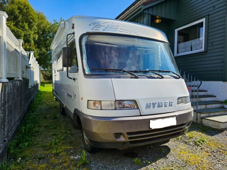 Camping-car blanc stationné près d’une maison verte