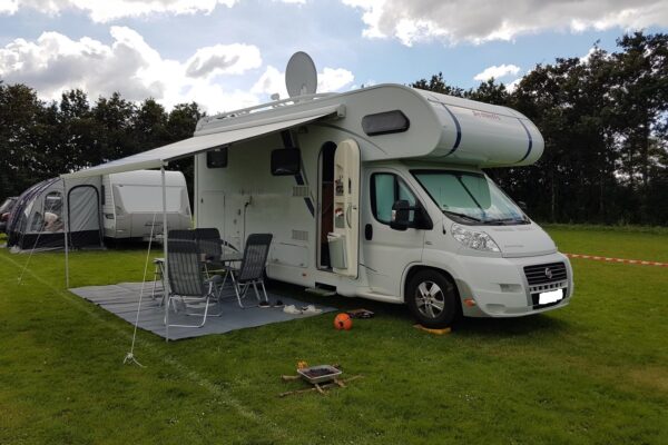 Camping-car avec auvent installé sur terrain herbeux