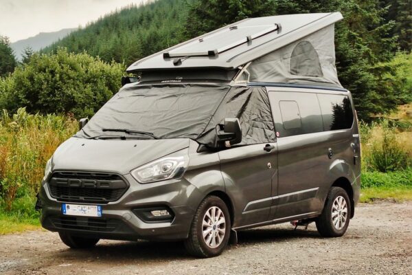 Van aménagé gris avec toit relevable en forêt