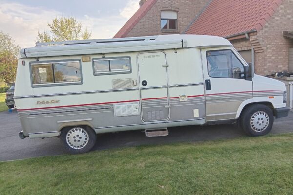 Camping-car Eriba blanc stationné devant maison en briques