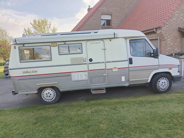 Camping-car Eriba blanc stationné devant maison en briques
