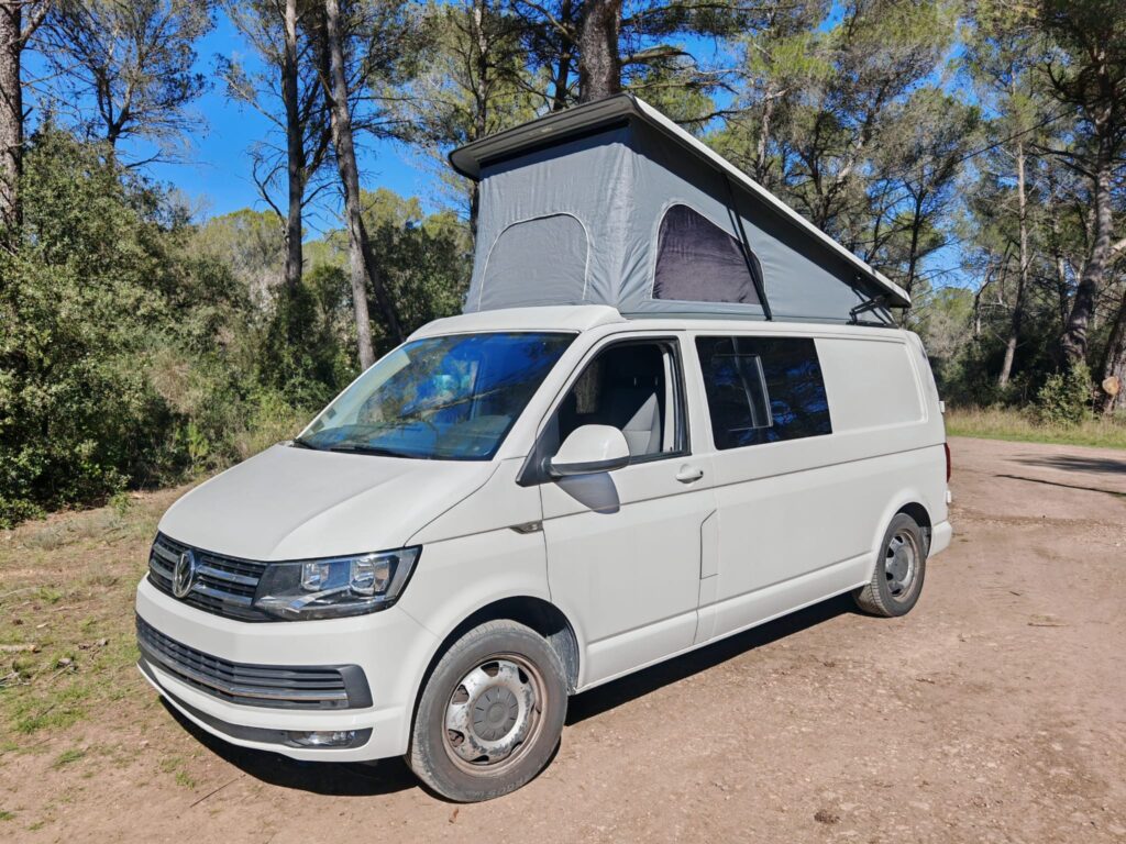 Van aménagé blanc avec toit relevable en forêt