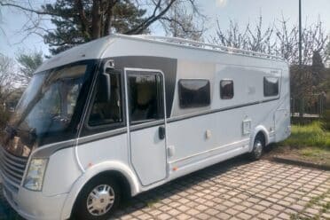 Camper bianco parcheggiato vicino agli alberi sotto il sole