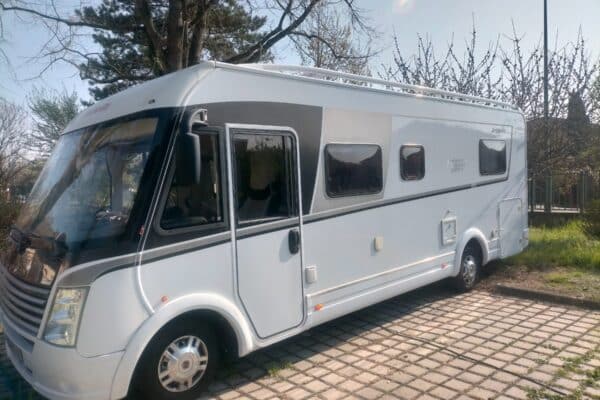 Camping-car blanc stationné près d'arbres au soleil