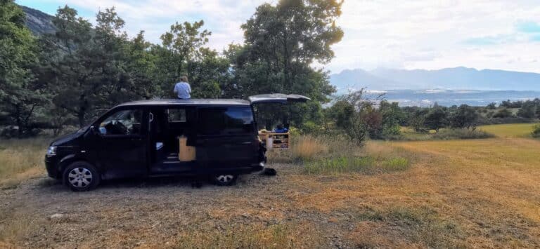 Van aménagé noir garé face aux montagnes