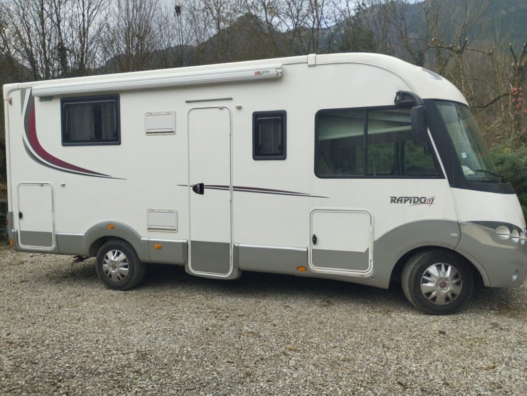 Camping-car blanc stationné sur terrain gravillonné