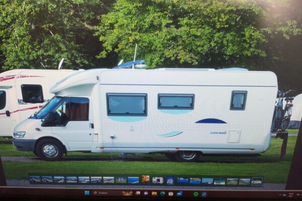 Camper bianco parcheggiato su prato con alberi