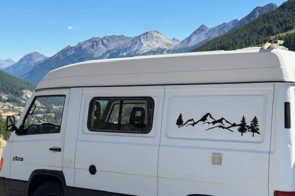 Van aménagé blanc devant des montagnes
