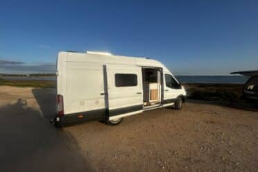 Van aménagé blanc face à la mer au soleil couchant