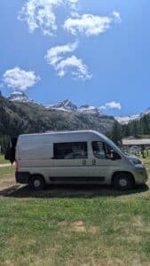 Van aménagé devant montagnes enneigées sous ciel bleu
