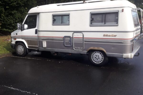 Camping-car blanc et gris stationné sur route humide