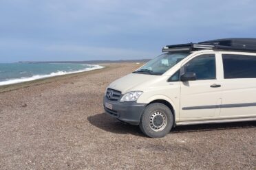 Van camperizzato beige parcheggiata sulla spiaggia di ghiaia