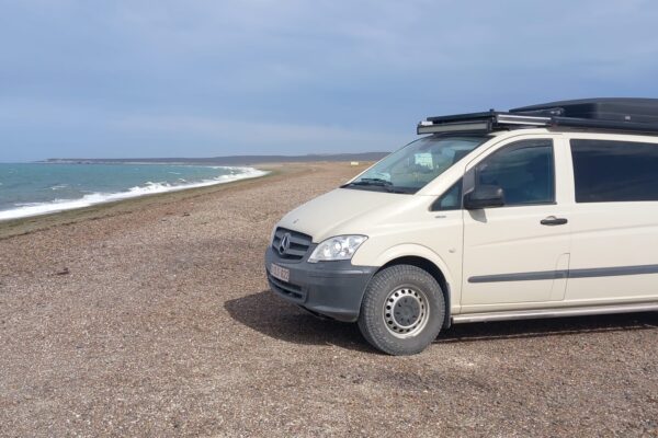 Van aménagé beige garé sur plage de galets