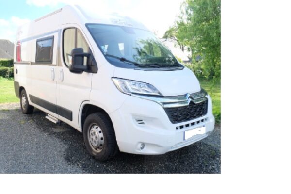 Fourgon aménagé blanc stationné sur terrain gravier