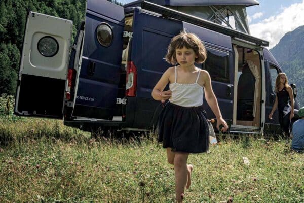 Mädchen geht in den Bergen neben einem van aménagé spazieren