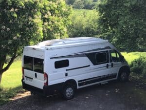 Camping-car blanc garé sous des arbres verdoyants