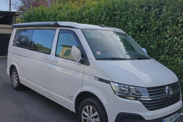 Van Volkswagen blanc garé devant haie verte